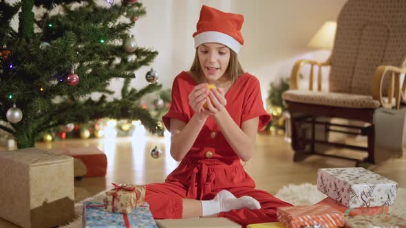 Relaxed Excited Teenage Girl Smelling Tasty Orange Sitting at Home on Christmas Eve