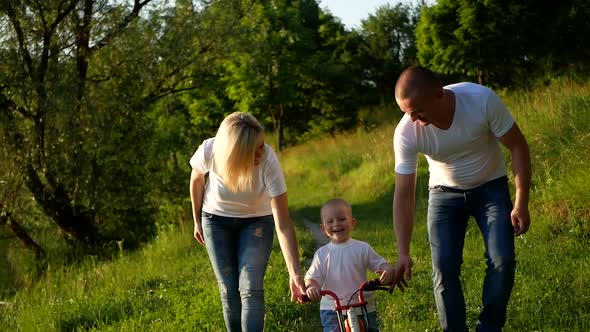 The Child Learns to Ride a Bike with His Parents in the Park