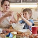 Young Mother with Little Son Kneading Dough and Forming It to Roll on Wooden Board - VideoHive Item for Sale
