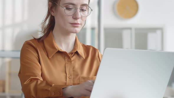 Young Female Office Worker in Glasses Typing on Laptop