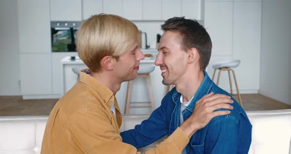Portrait of Two Happy Men Gay Couple in Love Kissing in Make a Gentle Headbutt While Sitting on Sofa