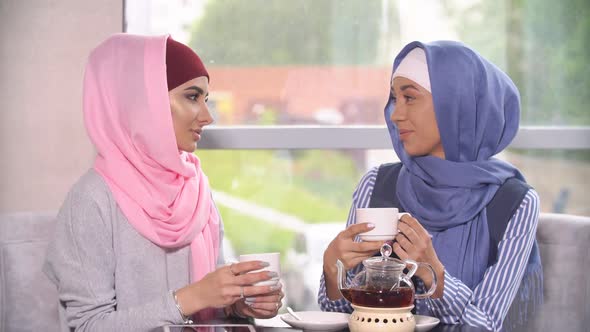 Two Beautiful Young Muslim Women in Cafe Communicate