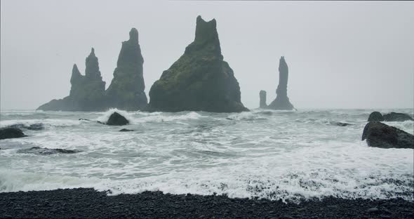 Sharp Cliffs on Black Sand Beach of Reynisfjara with Waves Hitting the Shore on Foggy Rainy Stormy