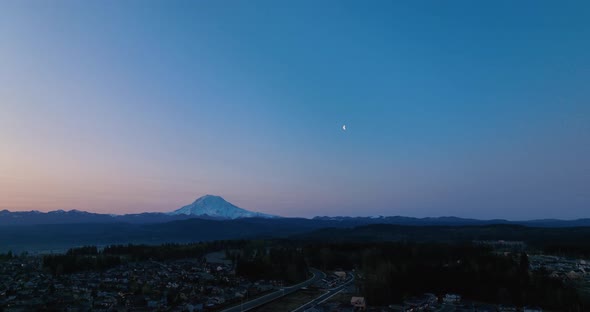 Aerial of Mount Rainier with the moon at sunrise.