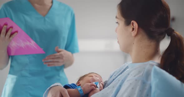 Happy Mother Holding Newborn Baby Talking to Doctor in Hospital