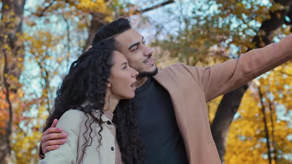 Happy Hispanic Young Couple Hugs in Autumn Park Joyfully Looking Into Distance Enamored Guy and Girl