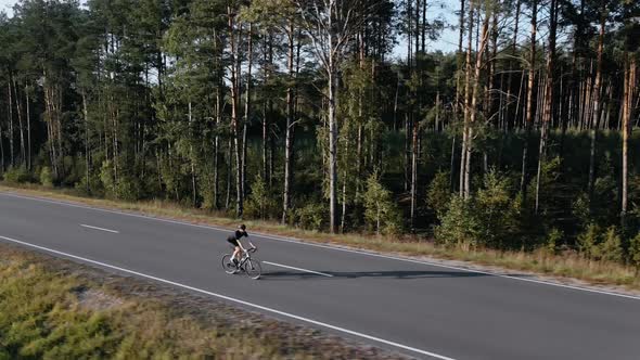 Drone Shot of Cyclist Riding a Road Bike on a Highway Near Field in Summer
