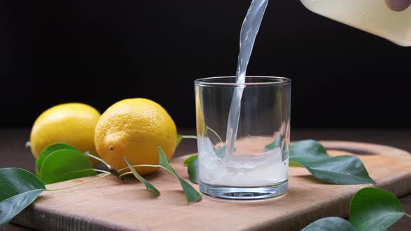 Man's hand pours lemon juice from pitcher into glass on wooden board