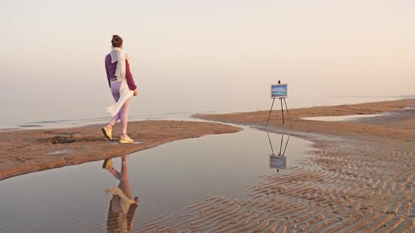 Elegant Woman with Hair Bun Walks Along Sand Spit To Easel