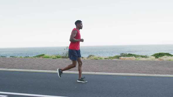 African american man exercising outdoors running on a coastal road