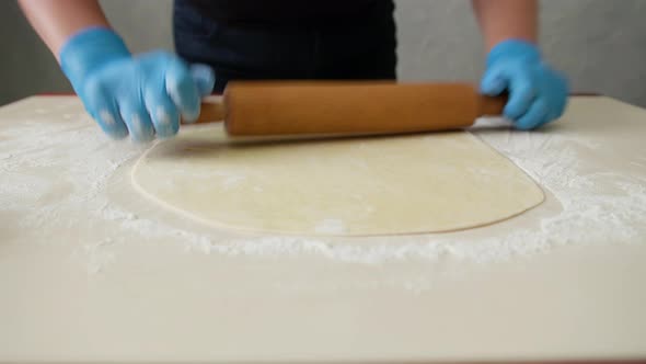 Rolls Out the Dough on the Kitchen Table. Female Hands Rolling Dough with a Rolling Pin, Close Up