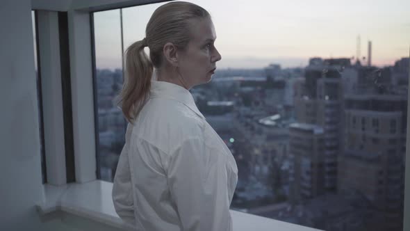 Side View of Confident Mid-adult Businesswoman Looking at Evening City Through Office Window