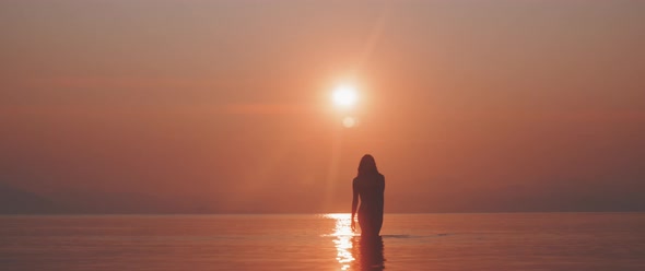 Silhouette of a woman walking in a calm sea towards the camera