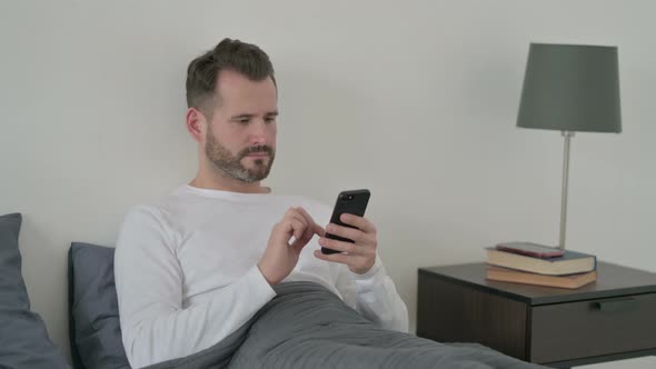 Man Celebrating Success on Smartphone in Bed