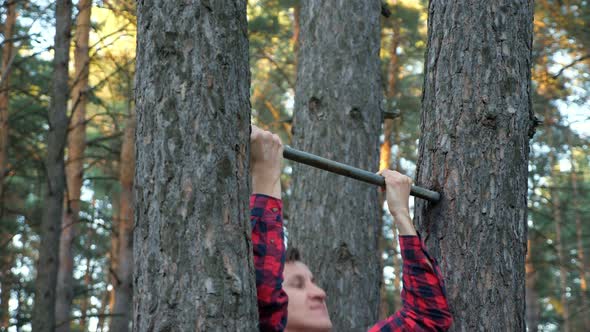Man in a Plaid Shirt Pulls Himself Up on a Horizontal Bar in the Forest