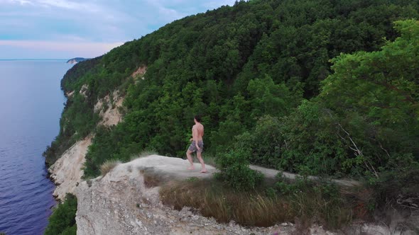 Young Shirtless Man Free Man Running to a Cliff and Raises His Hands Apart