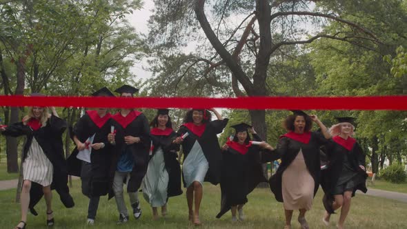 Carefree Multiethnic Diverse Graduates with Diplomas Running to Cross Finish Line Outdoors