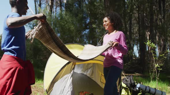 Smiling diverse couple packing equipment after camping in countryside