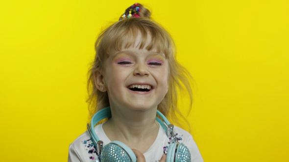 Child Smiling, Looking at Camera, Girl with Headphones on the Neck Posing on Yellow Background