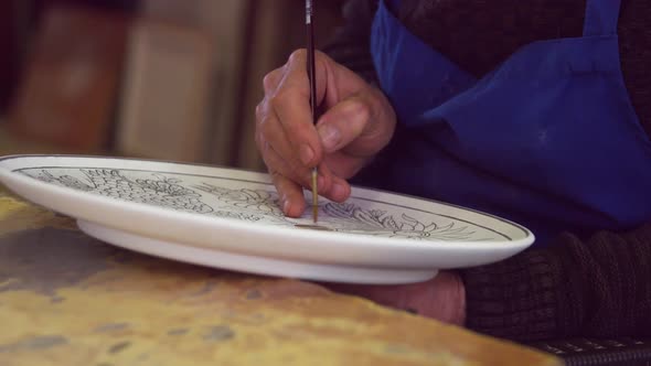 The master is painting the plate. Tile art.