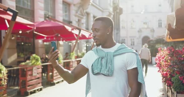 Guy in Stylish Clothes which Has Video Call while Walking in the City with Cozy Street Cafes