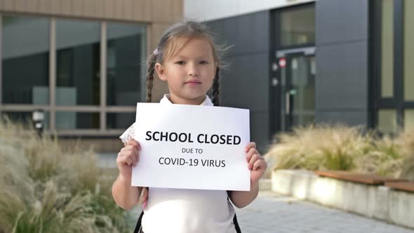 Cute Little Schoolgirl with Pigtails Stands with a Poster SCHOOL IS CLOSED DUE TO COVID19 VIRUS