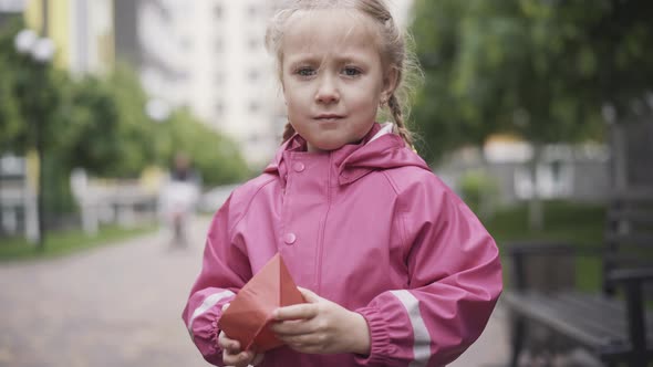 Portrait of Beautiful Little Caucasian Girl Posing with Paper Boat Outdoors. Cute Blond Kid in Pink