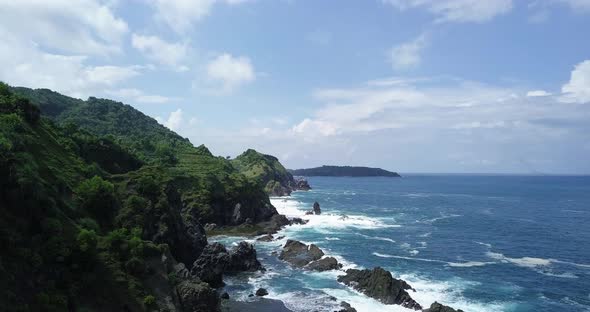 Ascending aerial shot of rocky coastline with crashing waves of ocean during sunny day - Indonesia,A