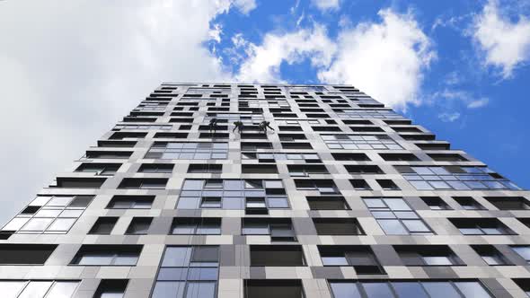 Industrial Climbers Cleaning the Exterior Windows of a Business Center with Blue Sky and Clouds on