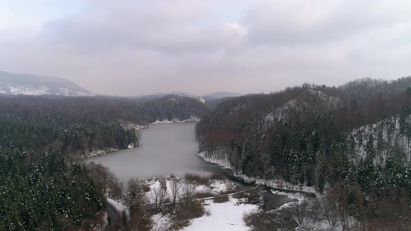 Aerial view of frozen lake surrounded with forest and fairy tale castle in the distance at winter