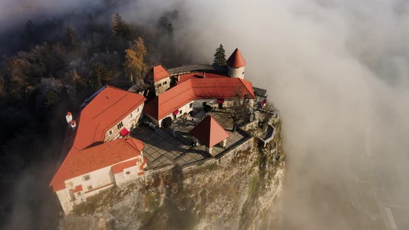 Golden hour aerial view over Bled castle, surrounded by morning clouds