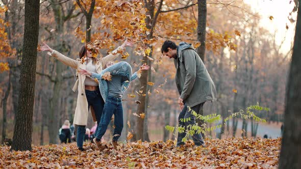 Young Mother Father and Little Daughter Laughing Fooling Around and Throwing Up Yellow Foliage While