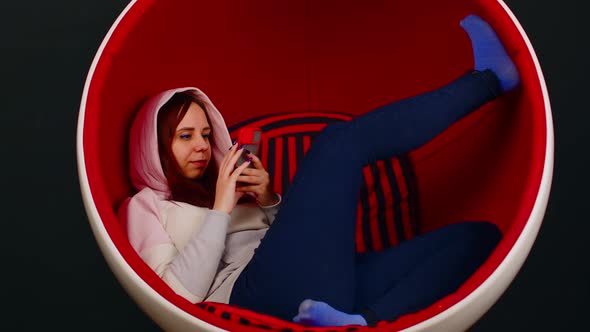 Young Woman with Mobile Phone Sitting in Ball Chair on Black Background