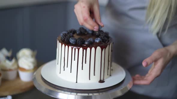 Young lovely woman pastry chef preparing birthday cake decorating with berries at home in kitchen