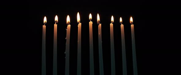 Lit Hanukkah candles burning in a dark room, slow motion