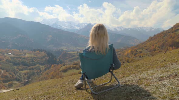 A woman sits on a chair and watches the mountain valley in autumn.
