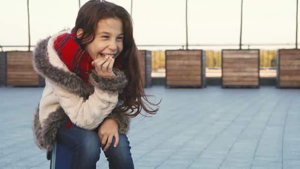 A Happy Girl Laughs Hard While Sitting on the Street