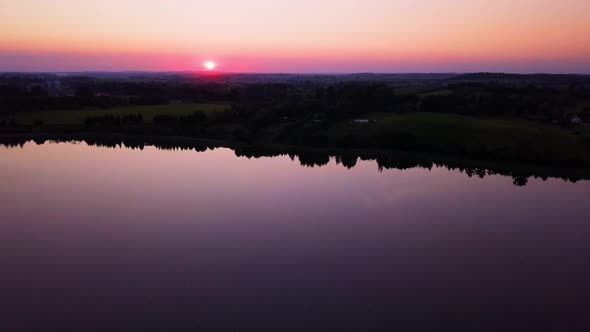 Colorful sunset over a peaceful lake, sarrounded by trees. Drone shot. Relaxing scenery.