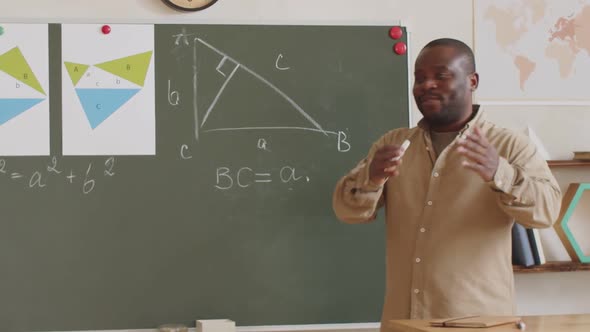 Black School Teacher Using Chalkboard and Explaining Lesson at Camera