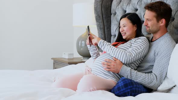 Man and pregnant woman looking at sonography in bedroom