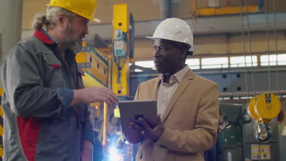 Diverse Engineers Using Tablet and Discussing Work in Factory