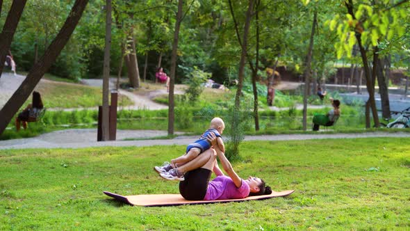 Young Woman Holding Baby and Working Out in Park