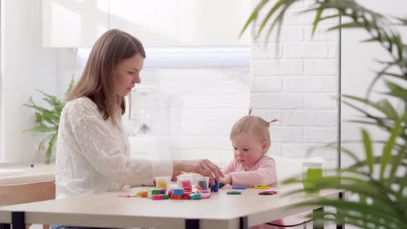 Mom and Little Daughter Sitting in Kitchen and Playing Multicolored Plasticine Mother and Daughter