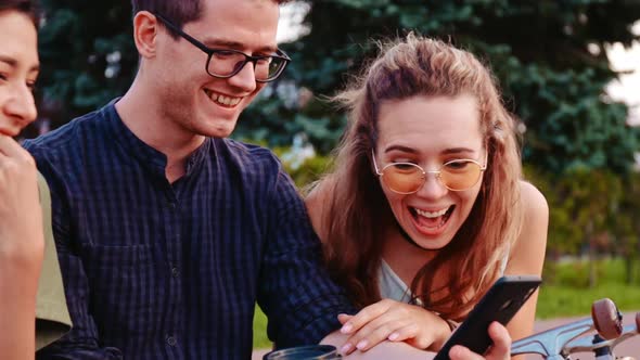 Happy Smiling Teenage Friends Laughing Outside at Something in Smartphone or Mobile Phone