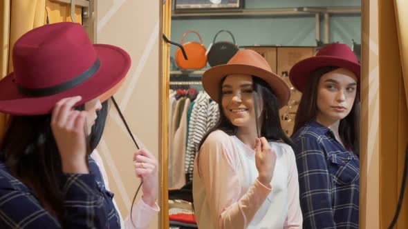 Two Young Lovely Women Trying on Hats, While Shopping Together