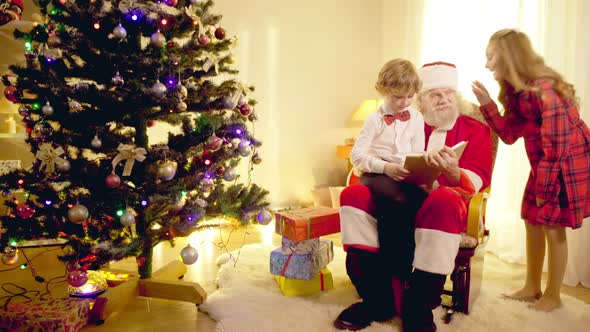 Wide Shot Smiling Father Christmas Reading Book with Children Listening