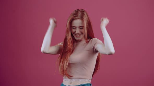 The Young Redhaired Girl in Profile Cheerful for 20 Years in a Pink Casual Tshirt Isolated on a Pink