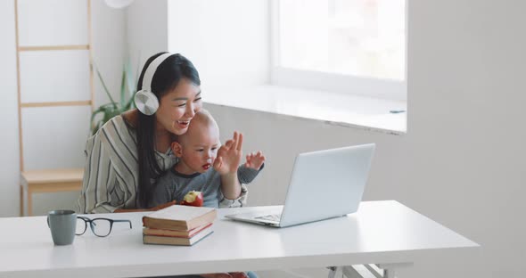 Young Mother Freelancer with Her Child Working at Home Office Using Laptop