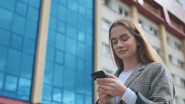 A Girl Walks Through Town and Looks at Her Smartphone