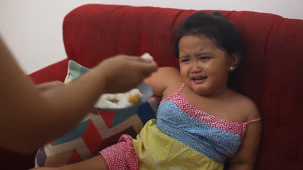 Cute asian little girl eating fed by her mother while crying at home